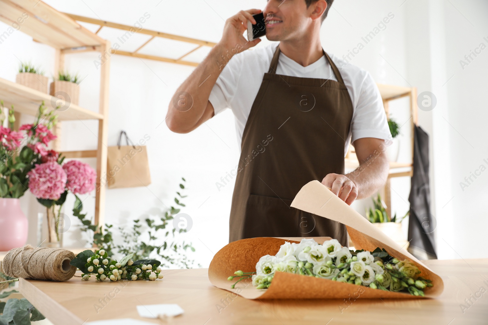 Photo of Florist with beautiful flowers talking on smartphone in workshop, closeup