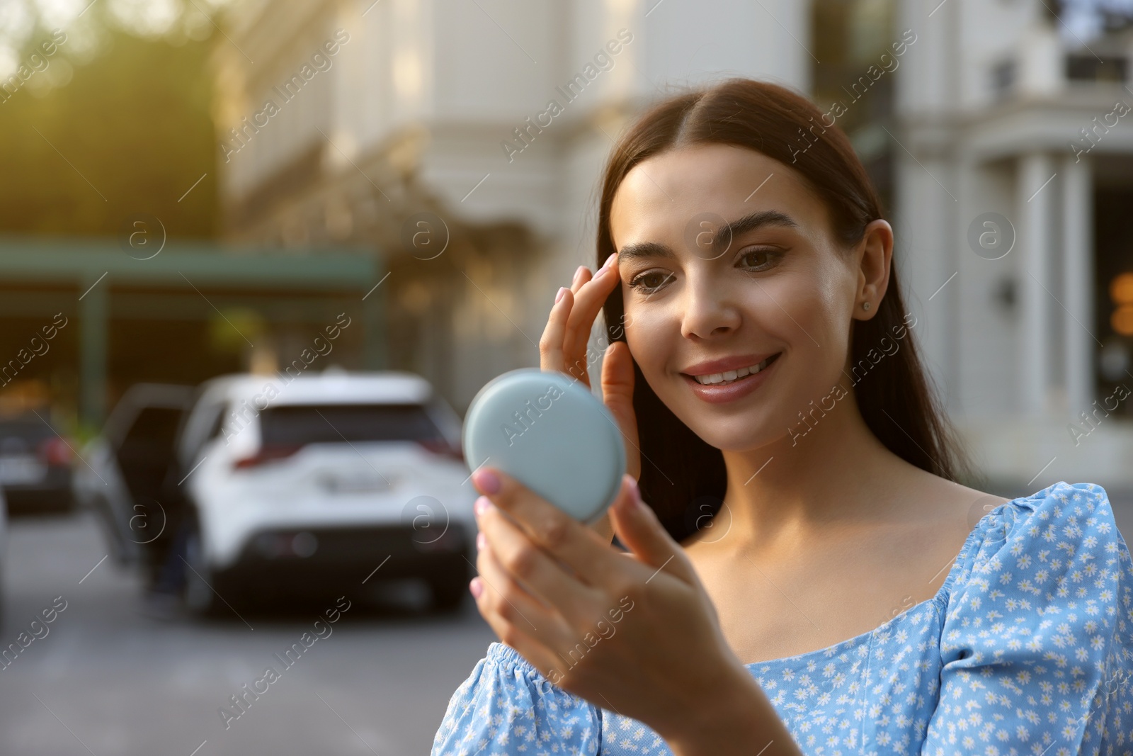 Photo of Beautiful young woman looking at herself in cosmetic pocket mirror outdoors. Space for text