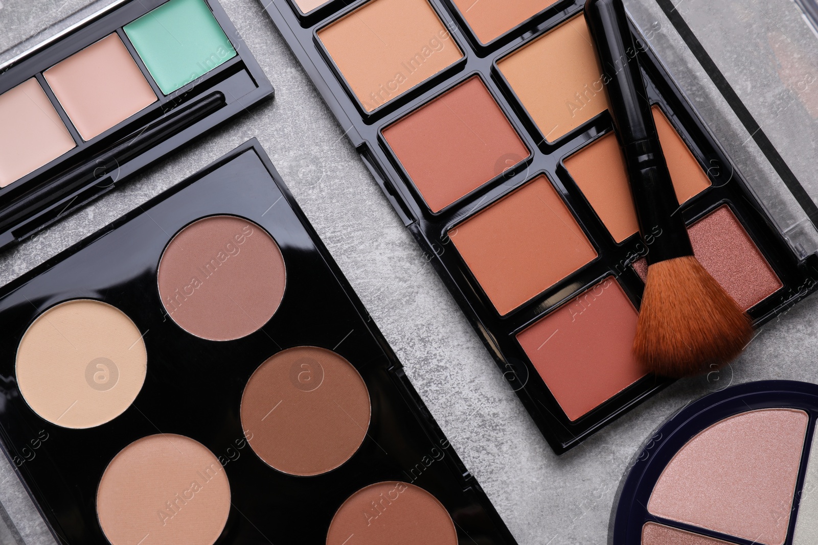 Photo of Different contouring palettes and brush on light gray background, flat lay. Professional cosmetic product