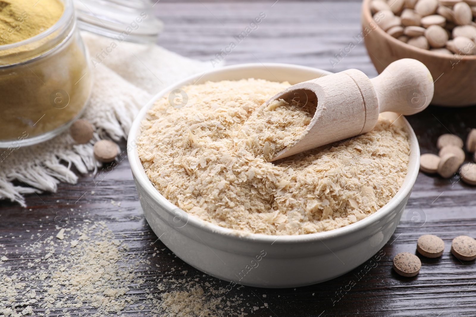 Photo of Bowl and scoop with brewer`s yeast flakes on wooden table