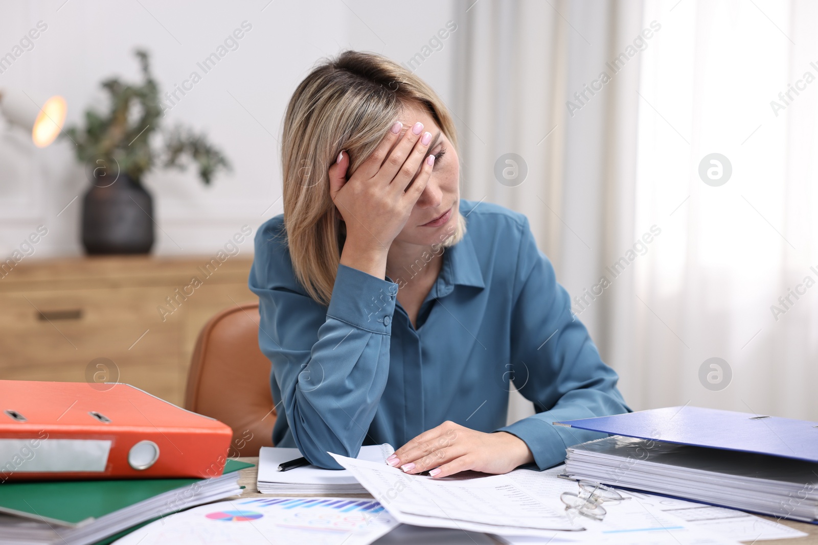 Photo of Overwhelmed woman sitting at table with documents in office