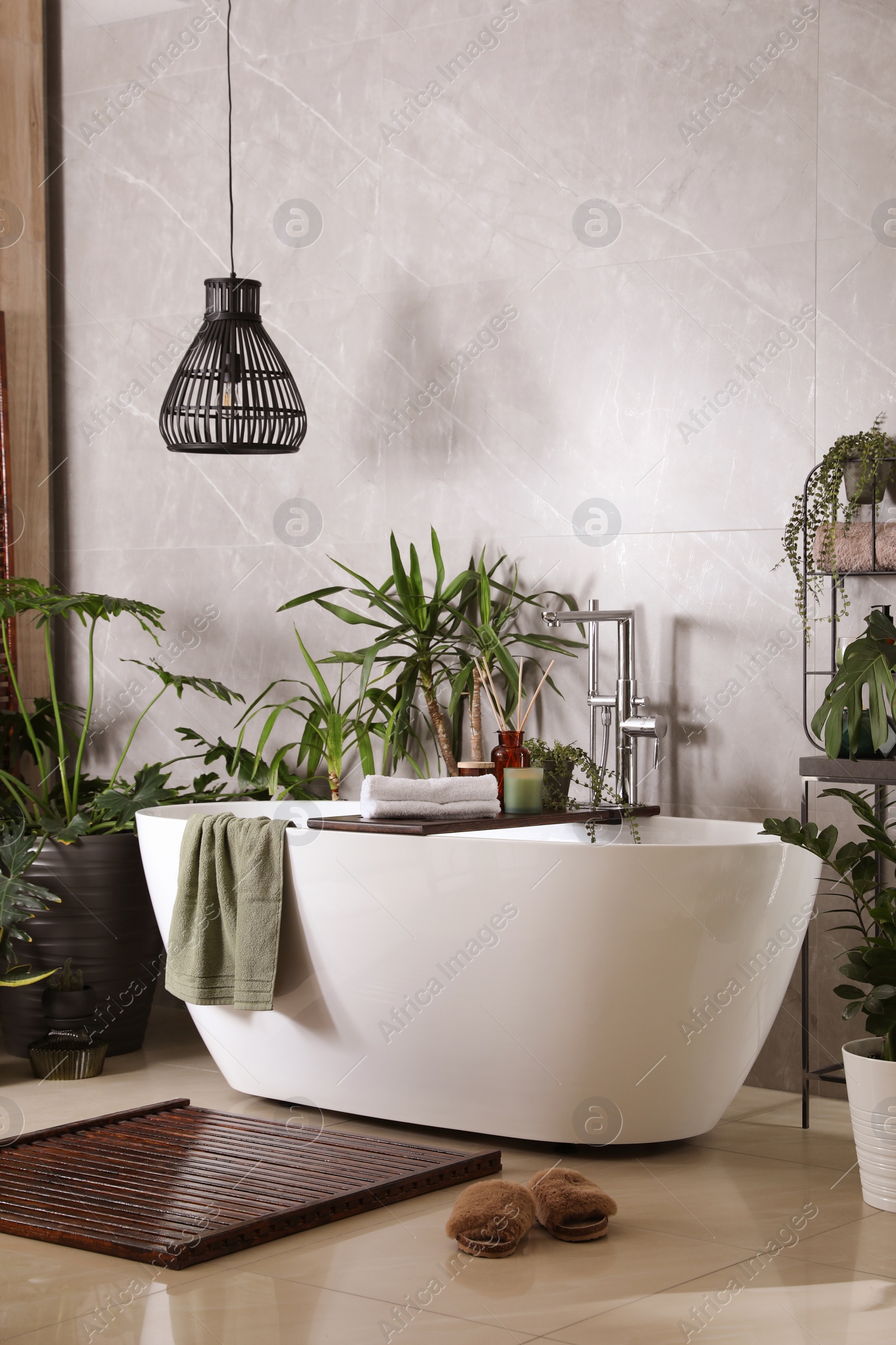 Photo of Modern white tub and beautiful green houseplants in bathroom. Interior design