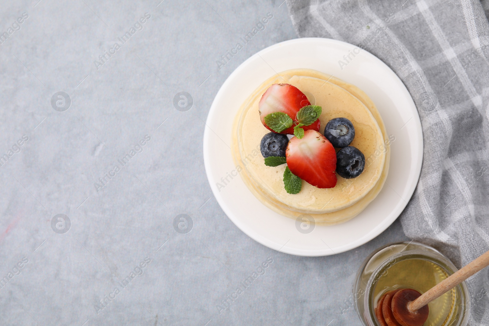 Photo of Stack of tasty pancakes with fresh berries, mint and honey on light grey table, top view. Space for text