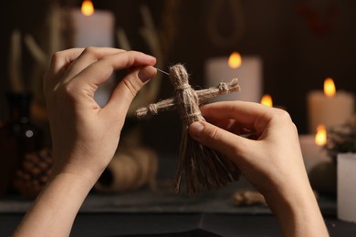 Photo of Woman stabbing voodoo doll with pin in dark room, closeup. Curse ceremony