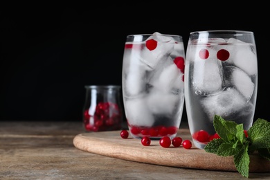 Glasses of cocktail with vodka, ice and cranberry on wooden table against black background. Space for text