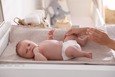Mother changing her baby's diaper on table in room