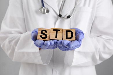 Photo of Doctor holding wooden cubes with abbreviation STD on grey background, closeup