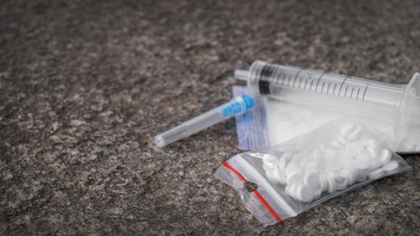 Photo of Plastic bag with powder, syringe and pills on stone surface, space for text. Hard drugs