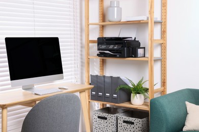 Photo of Modern printer on shelf near table with computer in home office