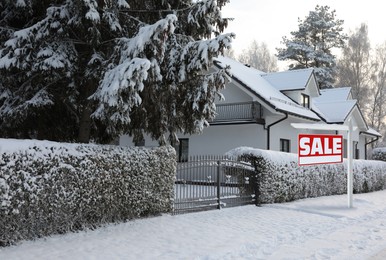 Sale sign near beautiful house outdoors in winter. Red signboard with word