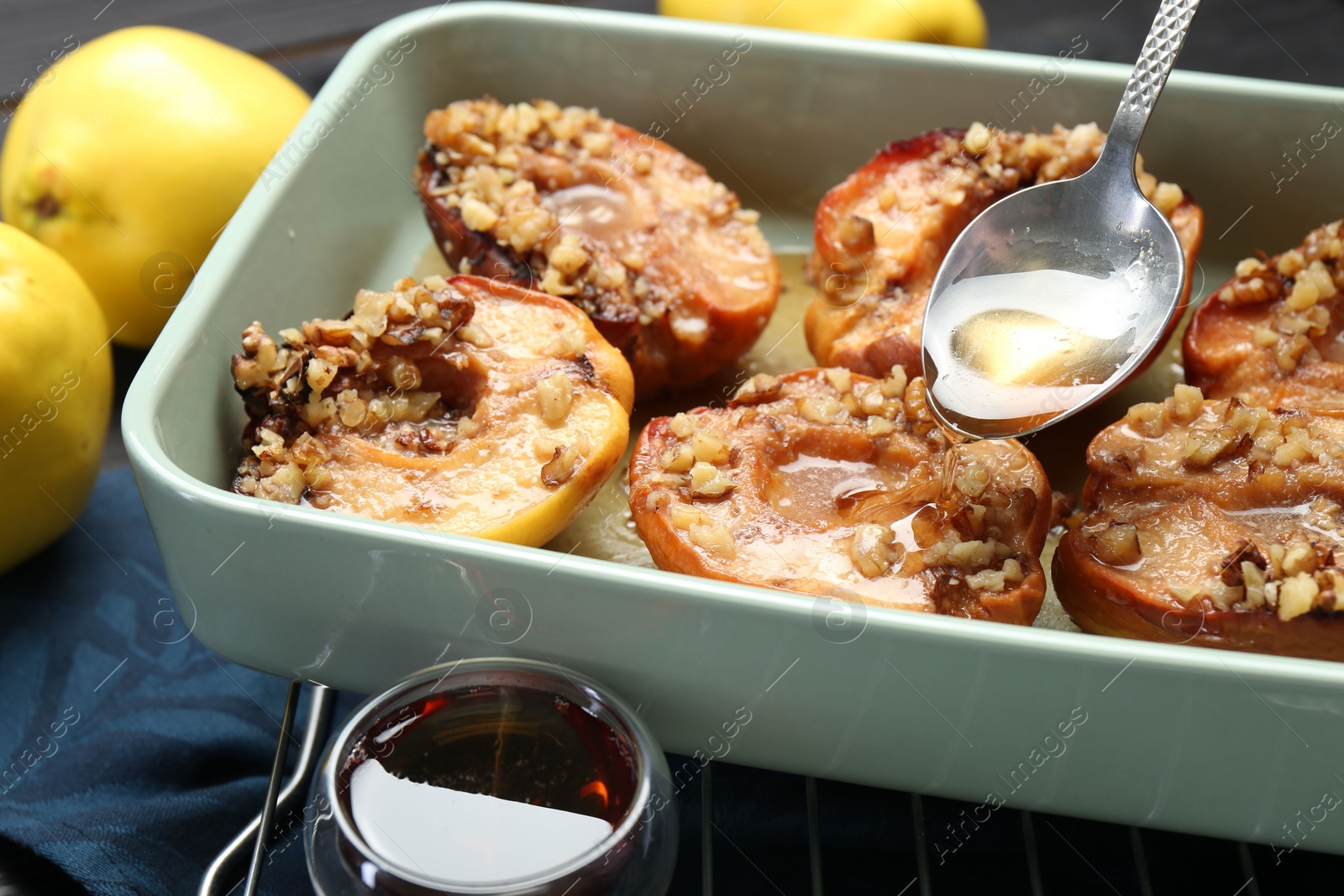 Photo of Pouring honey onto tasty baked quinces with nuts in dish at table, closeup