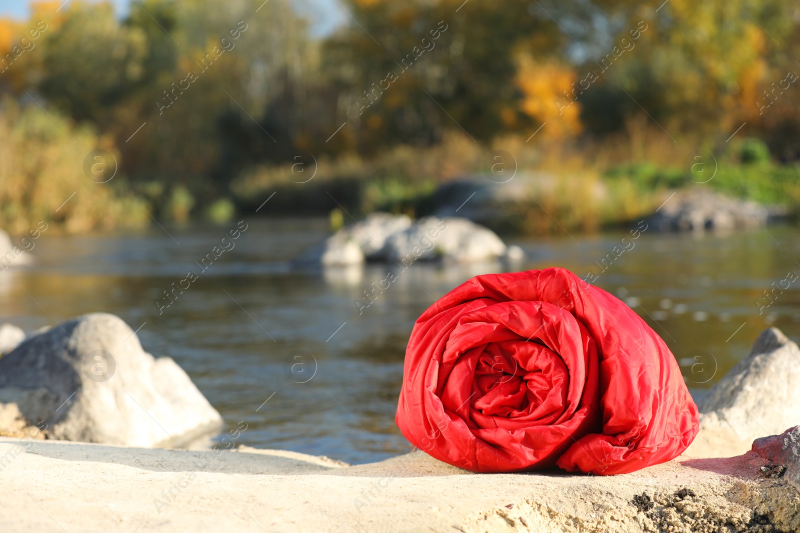 Photo of Red sleeping bag on ground outdoors, space for text. Camping equipment