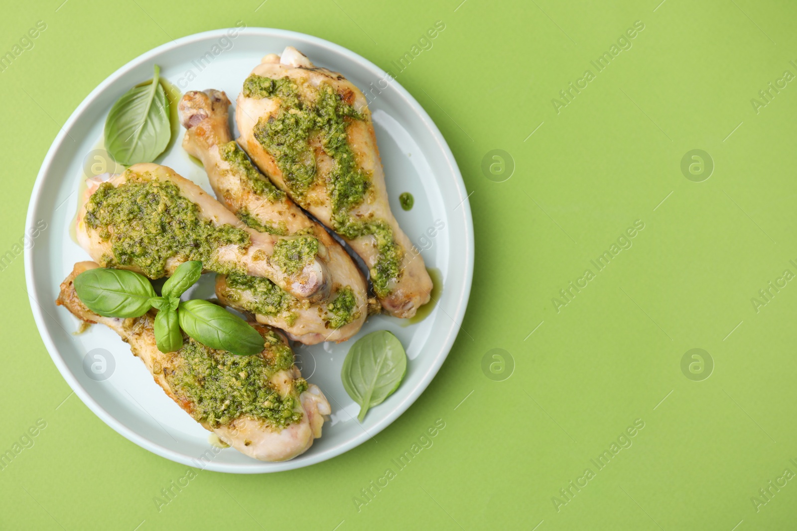 Photo of Delicious fried chicken drumsticks with pesto sauce and basil on green table, top view. Space for text