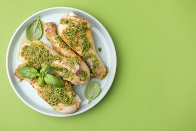 Photo of Delicious fried chicken drumsticks with pesto sauce and basil on green table, top view. Space for text