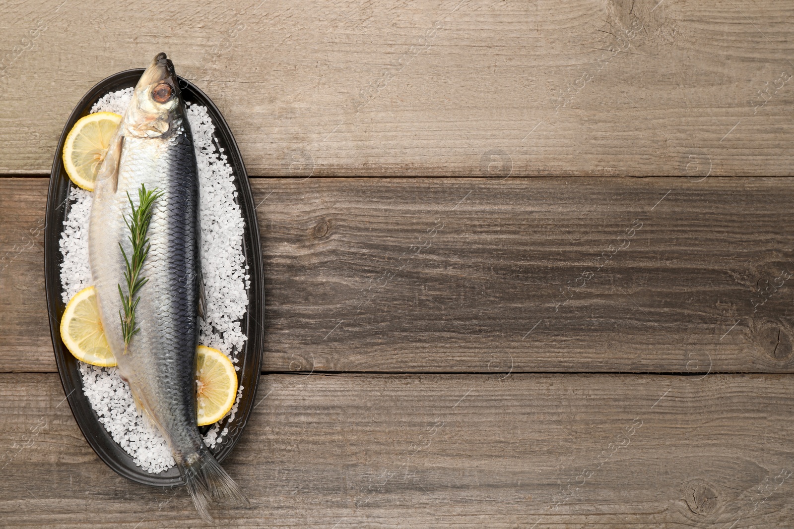 Photo of Plate with salted herring, rosemary and lemon on wooden table, top view. Space for text