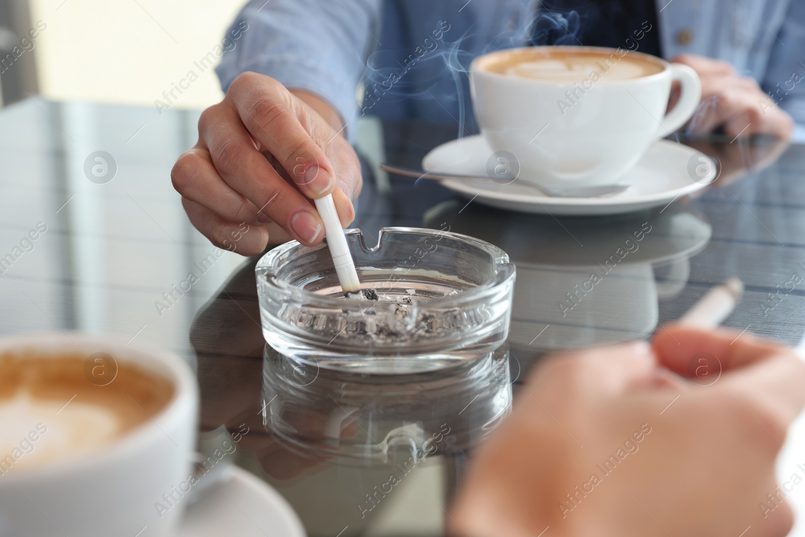 Photo of Woman putting out cigarette in ashtray at table, closeup