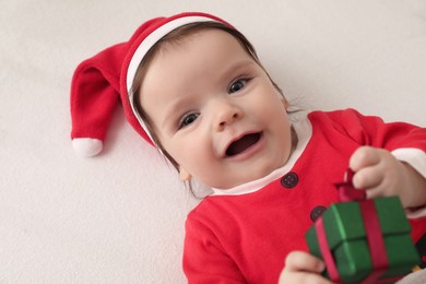 Photo of Cute baby wearing festive Christmas costume with gift box in crib, closeup