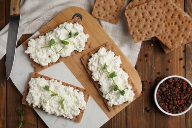 Photo of Crispy crackers with cottage cheese and microgreens on wooden table, flat lay