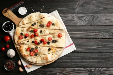 Delicious focaccia bread with olives and tomatoes on black wooden table, flat lay. Space for text