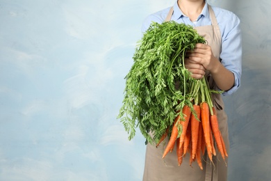 Photo of Woman holding fresh ripe carrots against color background. Space for text