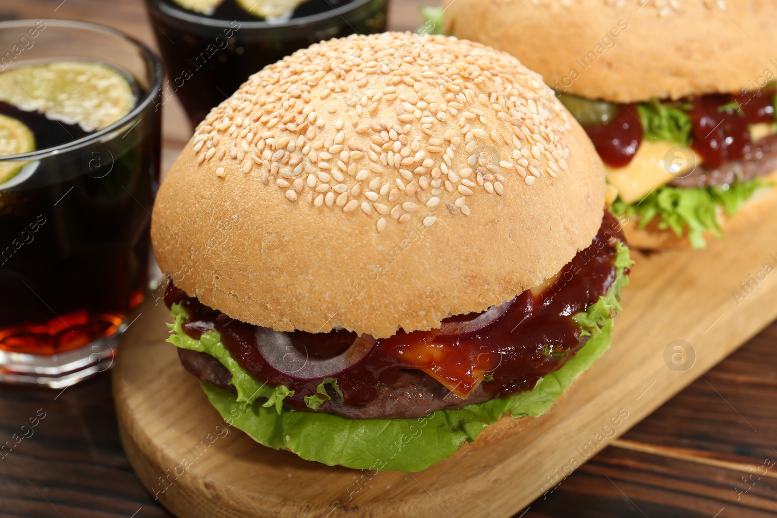 Photo of Delicious cheeseburgers and drinks on wooden table, closeup