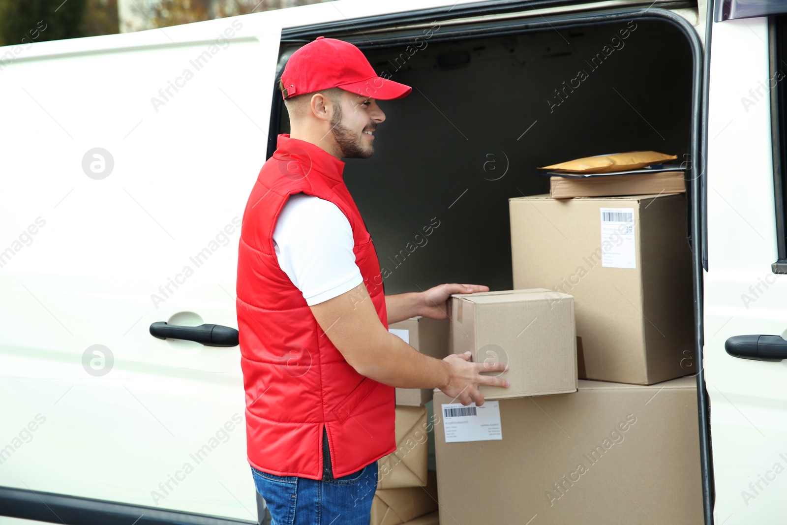 Photo of Young courier near van with parcels outdoors