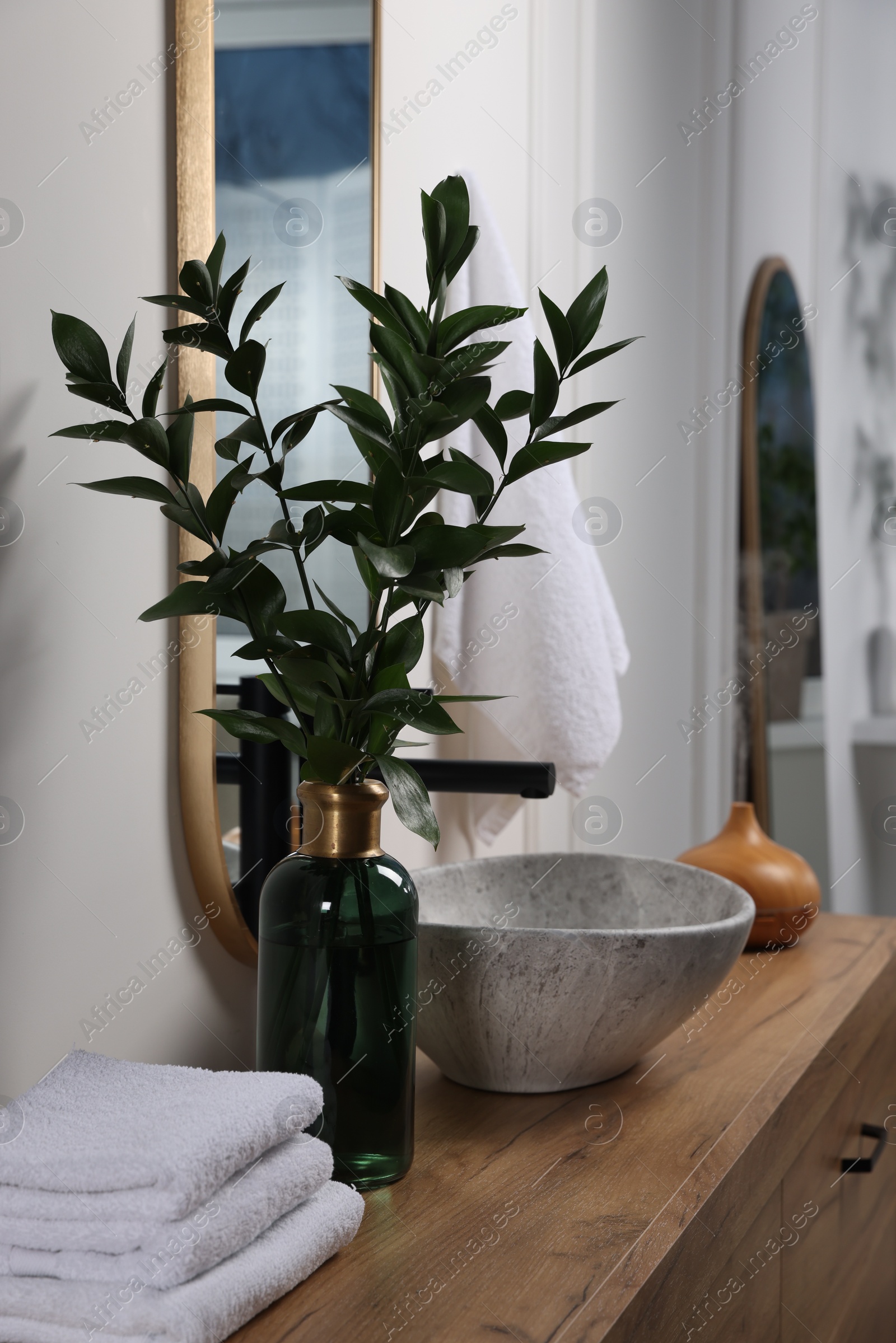 Photo of Eucalyptus branches and folded towels near stylish vessel sink on bathroom vanity. Interior design