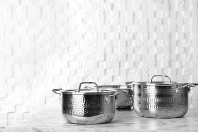 Photo of Clean saucepans and colander on table against white wall, space for text