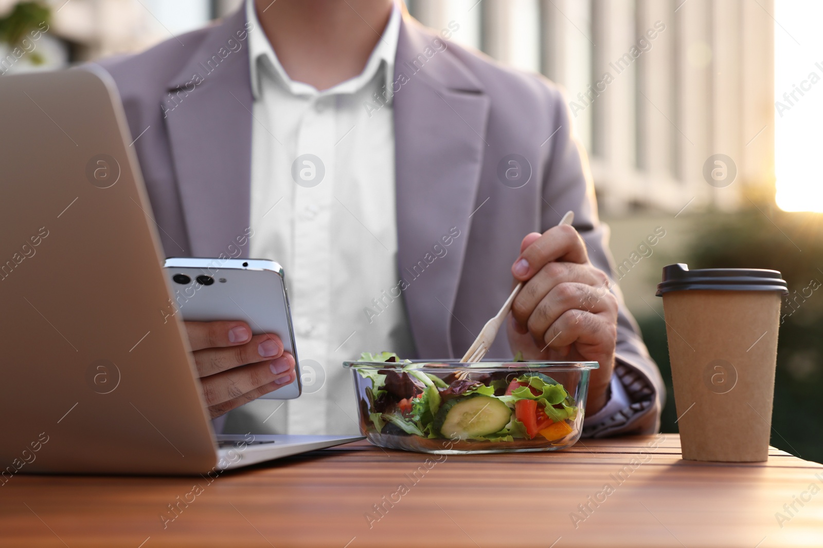 Photo of Businessman using smartphone during lunch at wooden table outdoors, closeup