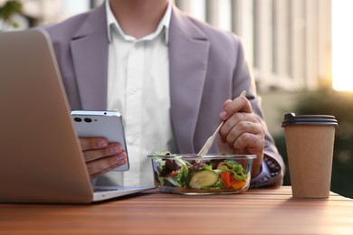 Photo of Businessman using smartphone during lunch at wooden table outdoors, closeup