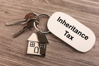 Photo of Inheritance Tax. Card and keys with key chain in shape of house on wooden table, top view