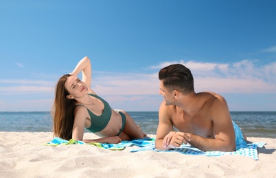 Photo of Woman in bikini and her boyfriend sunbathing on beach. Lovely couple