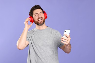 Photo of Happy listening music with headphones on violet background