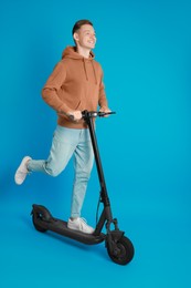 Happy man riding modern electric kick scooter on light blue background