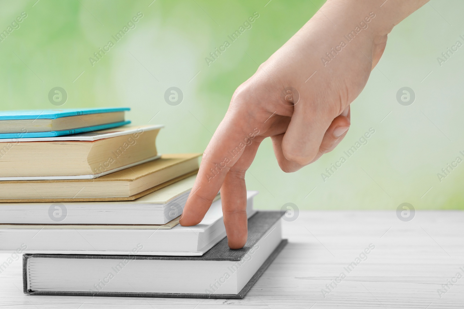 Photo of Man climbing up stairs of books with fingers on white wooden table against blurred background, closeup