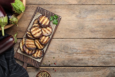 Photo of Delicious grilled eggplant slices on wooden table, flat lay. Space for text