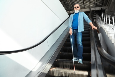 Photo of Blind person with long cane on escalator indoors. Space for text