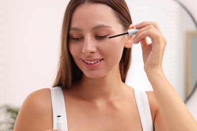 Photo of Beautiful woman applying serum onto eyelashes indoors