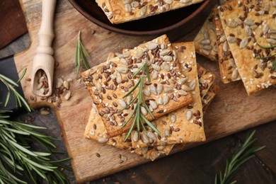 Photo of Cereal crackers with flax, sunflower, sesame seeds and rosemary on wooden table, top view