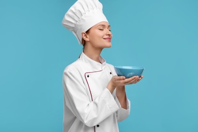 Photo of Happy chef in uniform holding bowl on light blue background