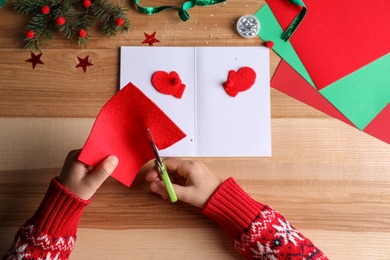 Little child making Christmas card at wooden table, top view