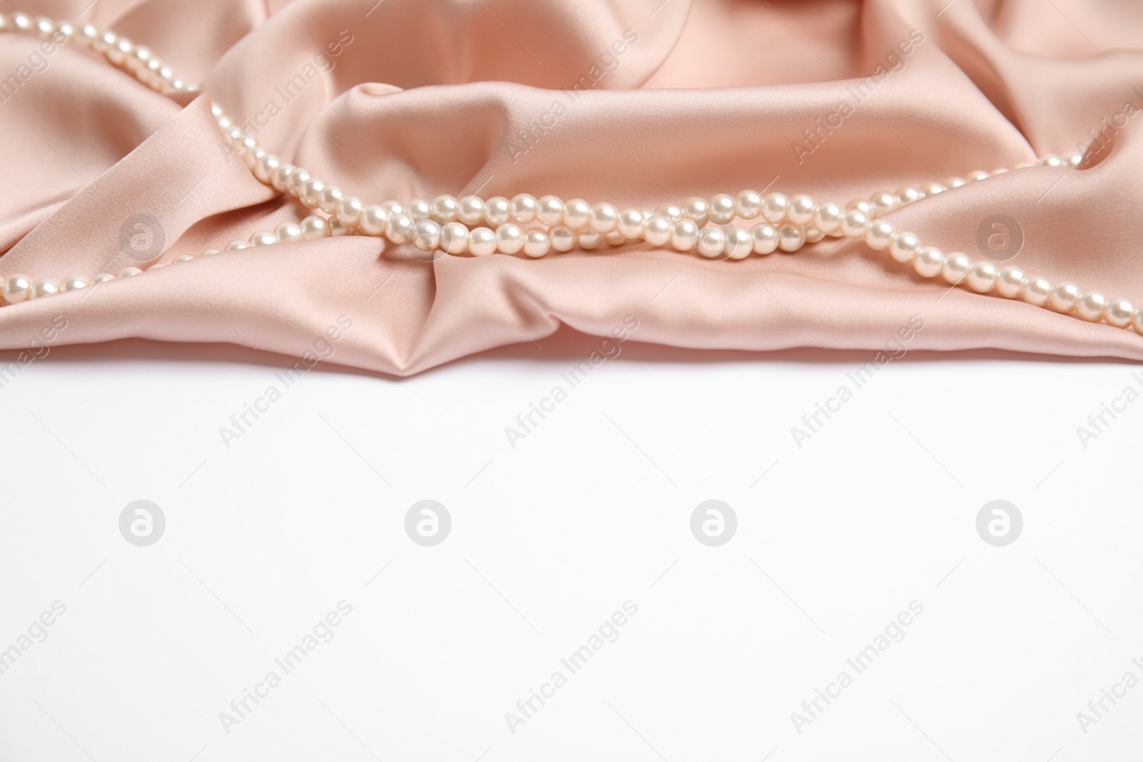 Photo of Beautiful pearls and pink silk on white background
