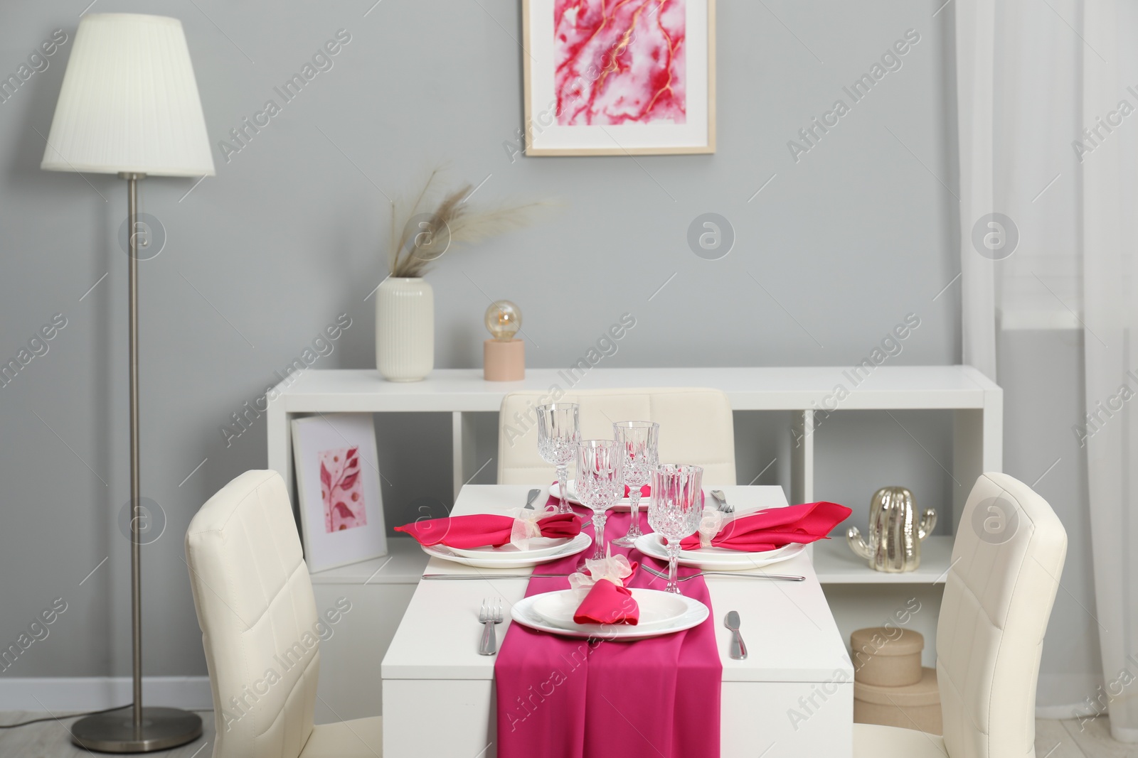 Photo of Color accent table setting. Glasses, plates, cutlery and pink napkins in dining room