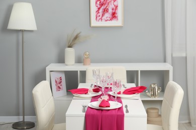 Color accent table setting. Glasses, plates, cutlery and pink napkins in dining room