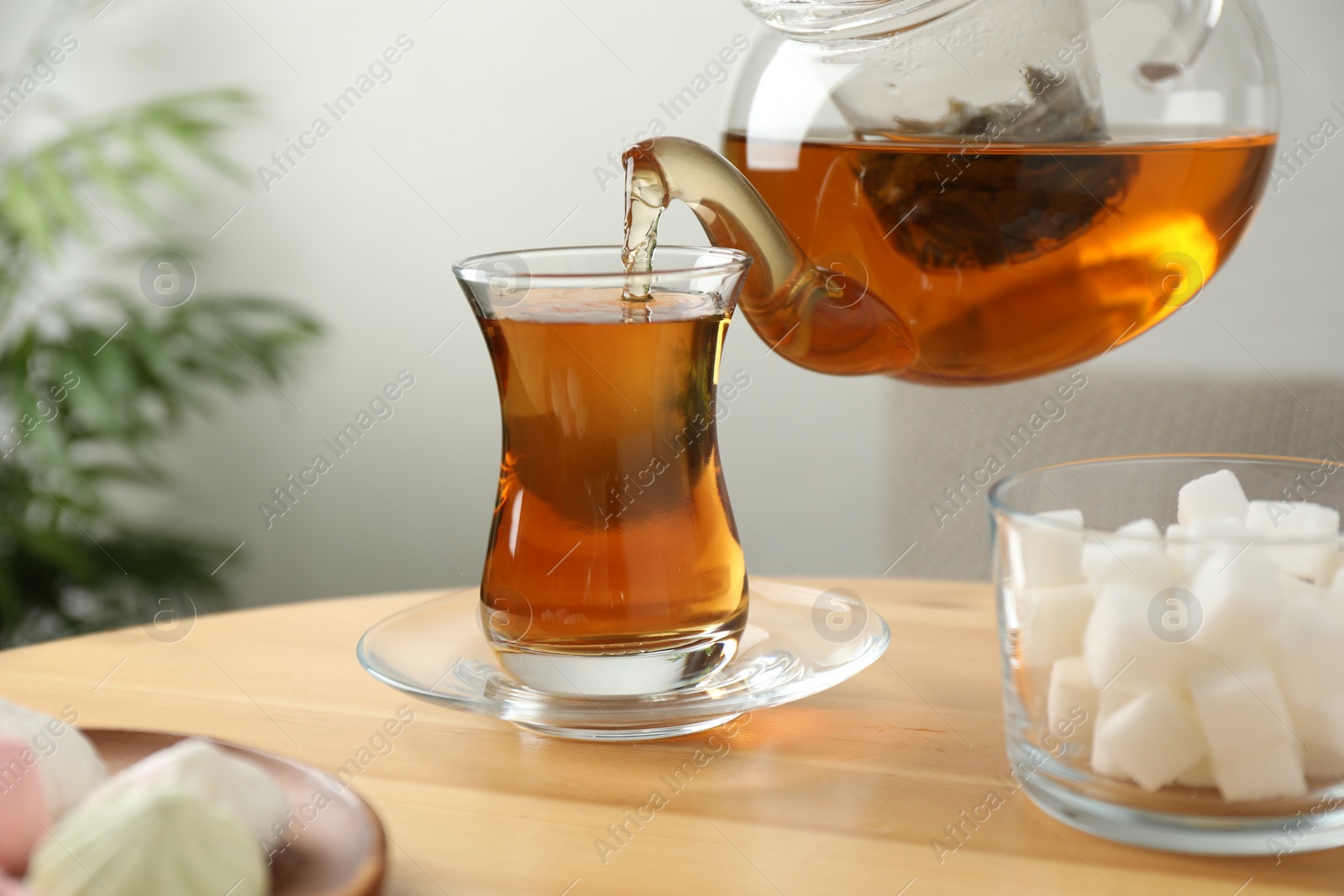Photo of Pouring tasty tea into cup at wooden table indoors
