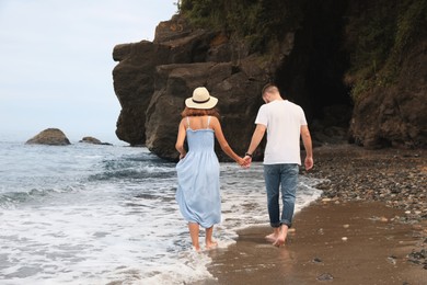 Photo of Young couple walking on beach near sea, back view