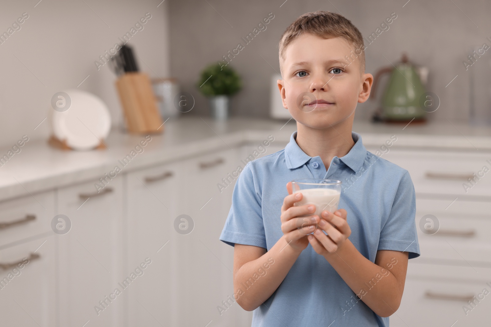 Photo of Cute boy with glass of fresh milk in kitchen, space for text