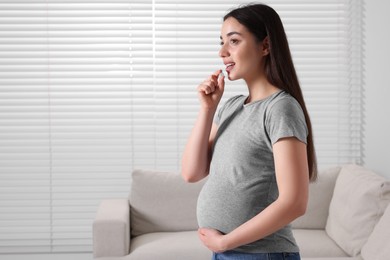 Pregnant woman taking pill at home, space for text