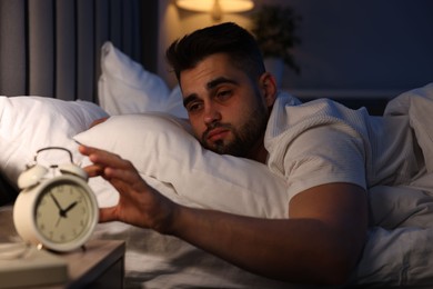 Photo of Sleepy man turning off alarm clock in bedroom