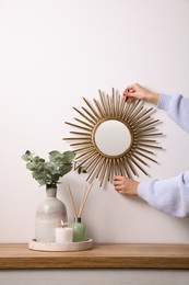 Photo of Woman hanging sun shaped mirror on white wall over wooden table, closeup